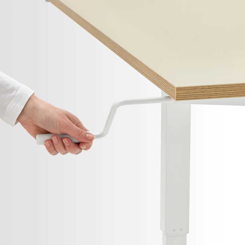 A human hand uses the handle on Skarsta Sit Stand Desk to manually adjust the height of the desk.