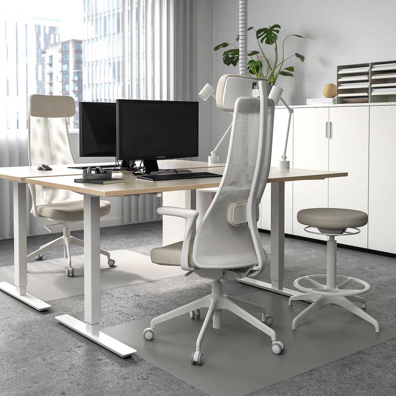 An ikea Skarsta Sit Stand Desk with white legs and beige top in an office enironment.